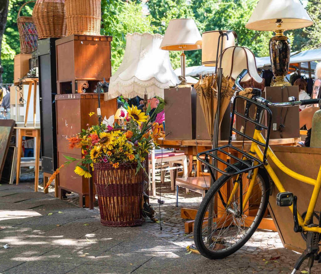 Furniture, a Lamp, a bike, and other miscellaneous items in a rummage sale on a parking lot shaded by a tree on a sunny day