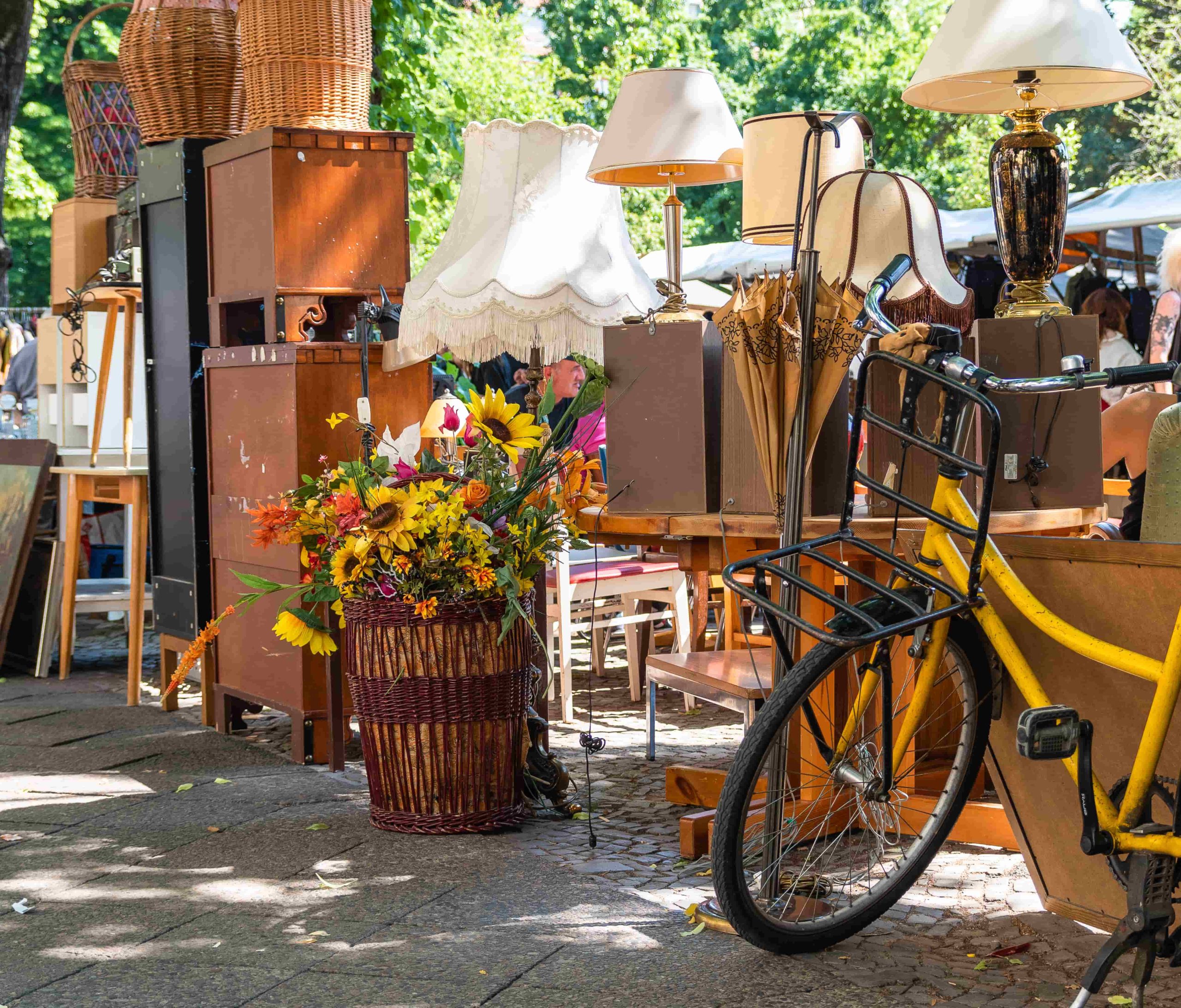 Furniture, a Lamp, a bike, and other miscellaneous items in a rummage sale on a parking lot shaded by a tree on a sunny day
